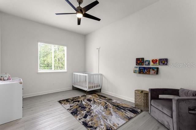 bedroom featuring a nursery area, hardwood / wood-style floors, and ceiling fan