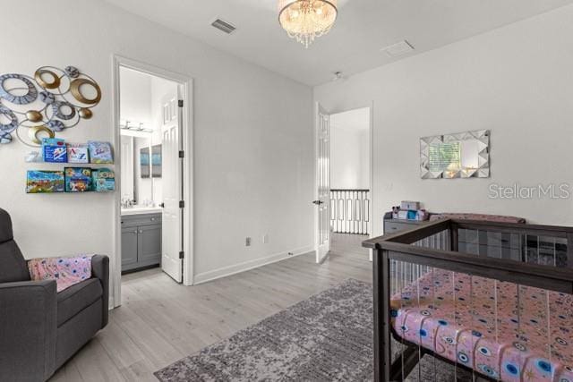 bedroom with connected bathroom, a chandelier, and light wood-type flooring