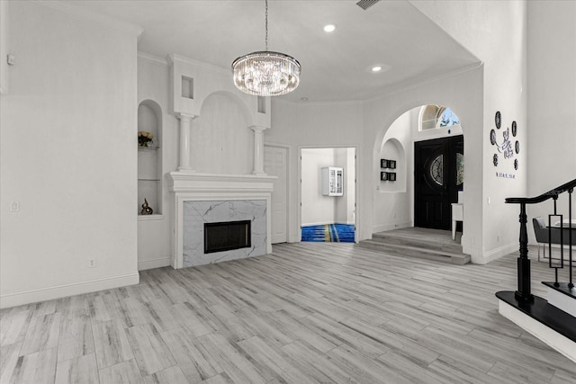 unfurnished living room with built in shelves, crown molding, an inviting chandelier, light hardwood / wood-style flooring, and a premium fireplace