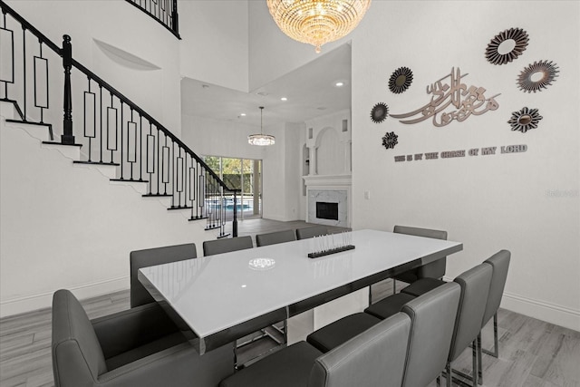 dining space with a towering ceiling, a high end fireplace, a chandelier, and light hardwood / wood-style floors