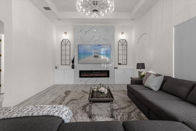 living room with a fireplace, wood-type flooring, a tray ceiling, and a notable chandelier