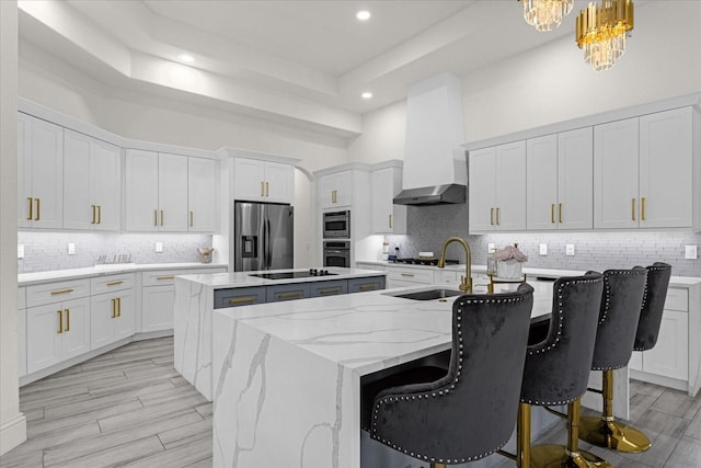 kitchen featuring white cabinetry, stainless steel fridge, hanging light fixtures, a kitchen island with sink, and wall chimney exhaust hood