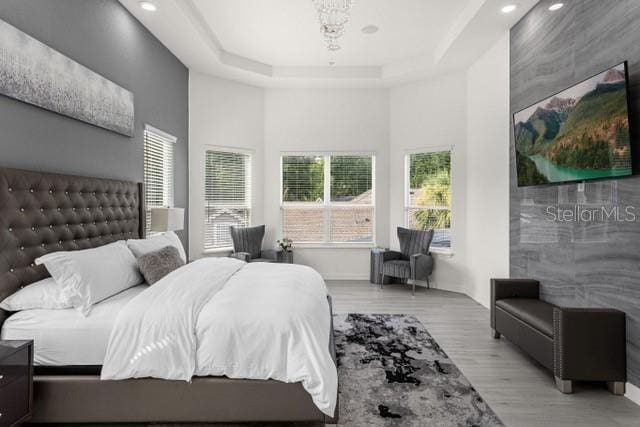 bedroom with a tray ceiling, a high ceiling, and light wood-type flooring