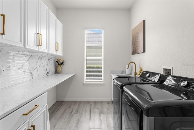 clothes washing area with cabinets, washing machine and dryer, and light hardwood / wood-style flooring