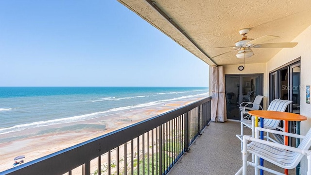 balcony with a beach view, ceiling fan, and a water view