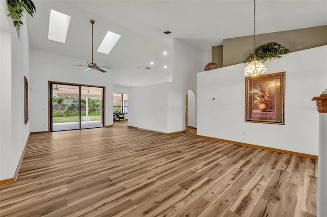 unfurnished living room featuring high vaulted ceiling, a skylight, ceiling fan with notable chandelier, and light hardwood / wood-style floors