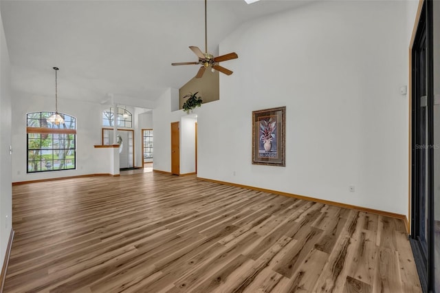 unfurnished living room with ceiling fan with notable chandelier, wood-type flooring, and high vaulted ceiling