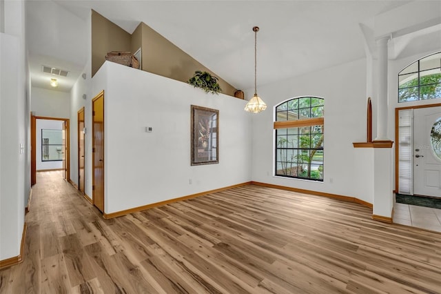 foyer entrance featuring high vaulted ceiling, light hardwood / wood-style flooring, ornate columns, and a notable chandelier