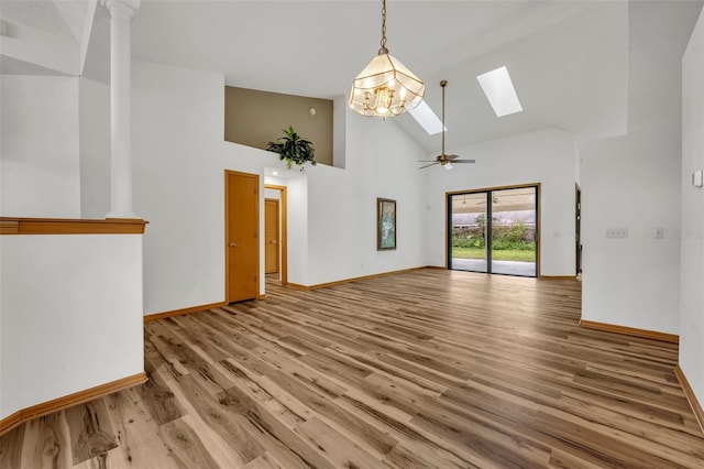 unfurnished living room featuring ceiling fan with notable chandelier, a skylight, a towering ceiling, and light wood-type flooring