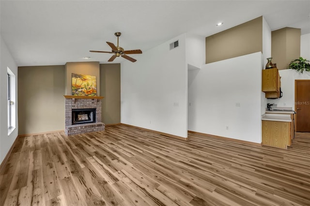 unfurnished living room with ceiling fan, vaulted ceiling, a fireplace, and light hardwood / wood-style flooring