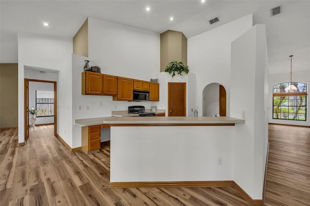 kitchen with light hardwood / wood-style floors, kitchen peninsula, decorative light fixtures, a towering ceiling, and black appliances