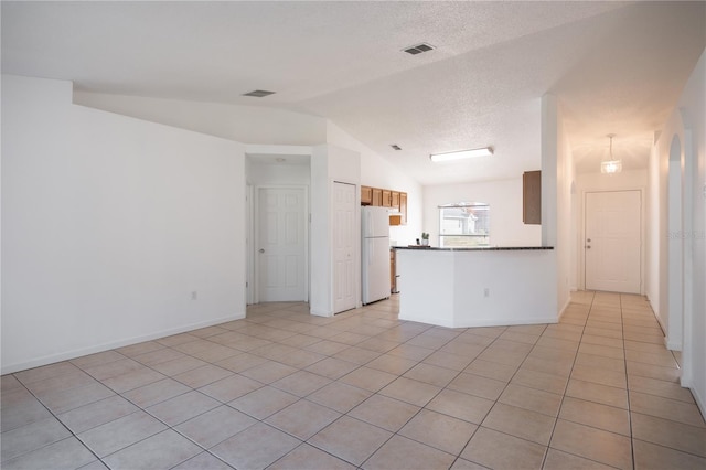 kitchen with lofted ceiling, a textured ceiling, light tile patterned floors, kitchen peninsula, and white fridge