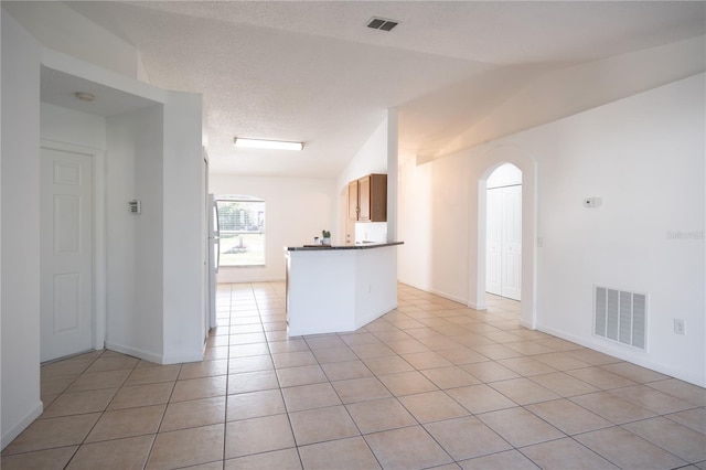 kitchen featuring vaulted ceiling, kitchen peninsula, a textured ceiling, and light tile patterned flooring