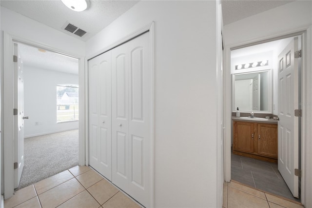 corridor with sink, light colored carpet, and a textured ceiling