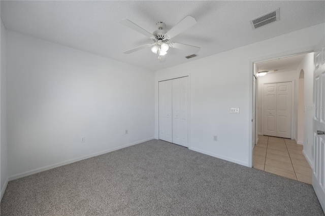 unfurnished bedroom with light colored carpet, a textured ceiling, ceiling fan, and a closet