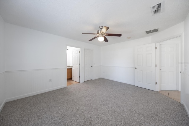 unfurnished bedroom with light colored carpet, ceiling fan, and ensuite bath