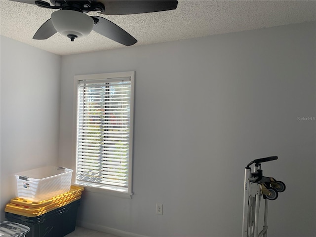 interior space featuring a ceiling fan, a textured ceiling, and baseboards