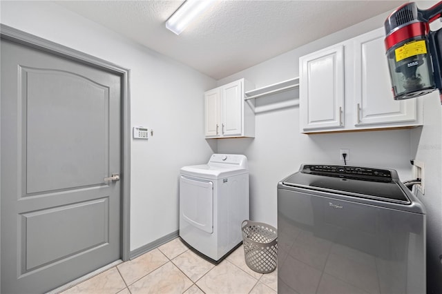 clothes washing area featuring cabinets, washer and dryer, light tile patterned floors, and a textured ceiling