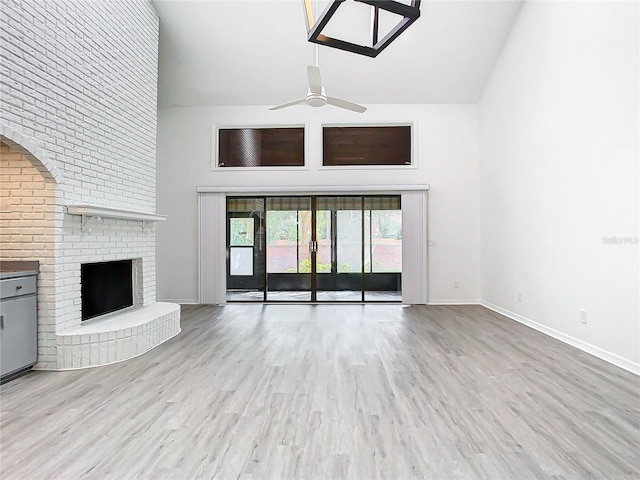 unfurnished living room with ceiling fan, light wood-type flooring, a high ceiling, and a brick fireplace