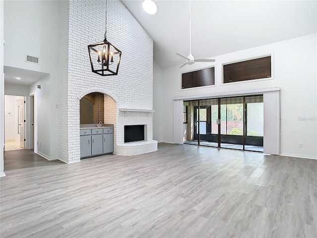 unfurnished living room with ceiling fan with notable chandelier, light wood-type flooring, a fireplace, and high vaulted ceiling