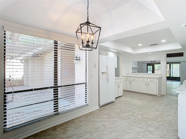 kitchen featuring white fridge with ice dispenser, hanging light fixtures, a raised ceiling, a chandelier, and white cabinets