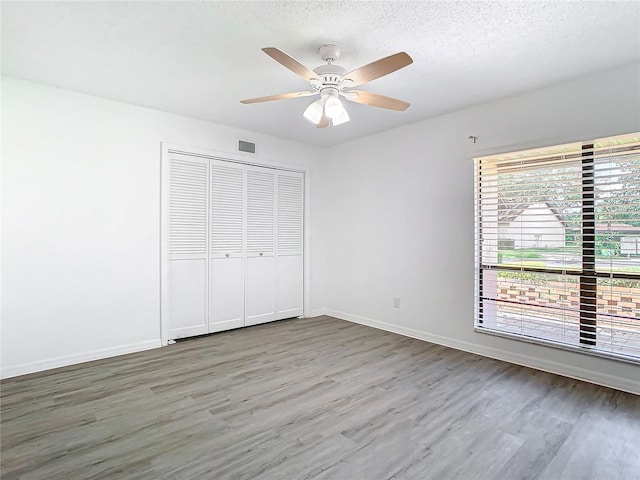 unfurnished bedroom featuring hardwood / wood-style floors, a textured ceiling, a closet, and ceiling fan