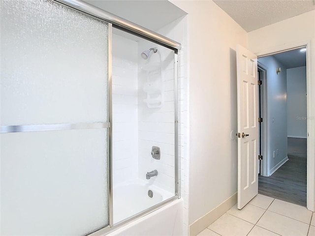 bathroom with tile patterned flooring, a textured ceiling, and combined bath / shower with glass door