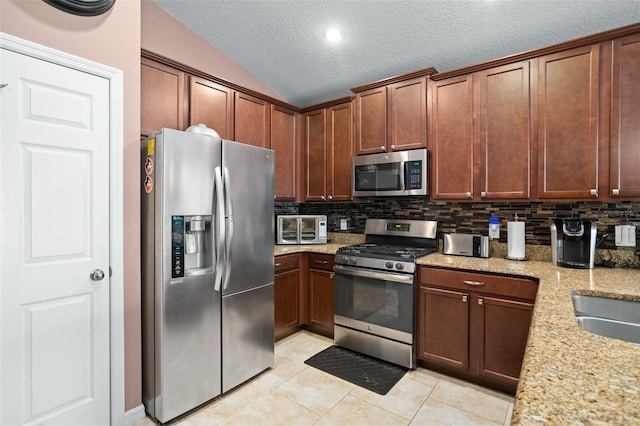 kitchen with light stone countertops, appliances with stainless steel finishes, tasteful backsplash, vaulted ceiling, and light tile patterned floors