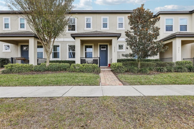 townhome / multi-family property featuring covered porch and a front yard