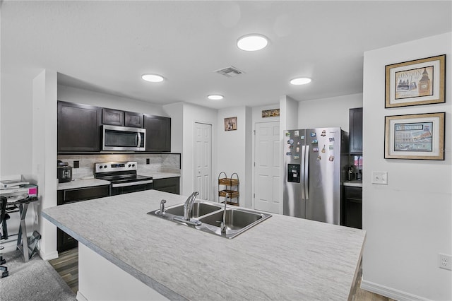 kitchen featuring backsplash, stainless steel appliances, sink, light hardwood / wood-style flooring, and an island with sink