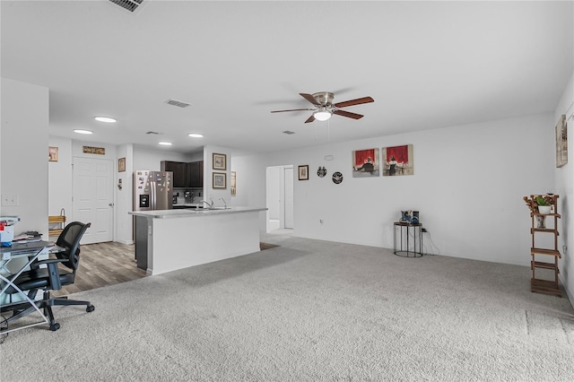 interior space with carpet, a kitchen island with sink, ceiling fan, sink, and stainless steel fridge with ice dispenser