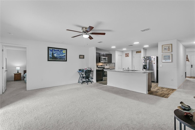 kitchen featuring ceiling fan, sink, stainless steel appliances, an island with sink, and carpet