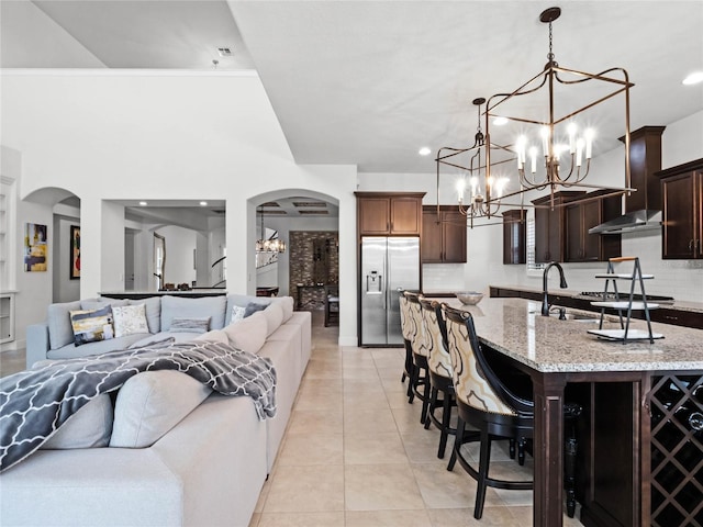 kitchen featuring dark brown cabinetry, light stone counters, decorative light fixtures, stainless steel fridge with ice dispenser, and a kitchen breakfast bar