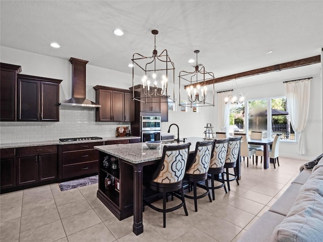 kitchen featuring wall chimney range hood, a breakfast bar, appliances with stainless steel finishes, dark brown cabinets, and a center island with sink