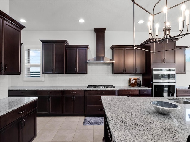 kitchen featuring pendant lighting, light stone countertops, stainless steel appliances, and wall chimney exhaust hood