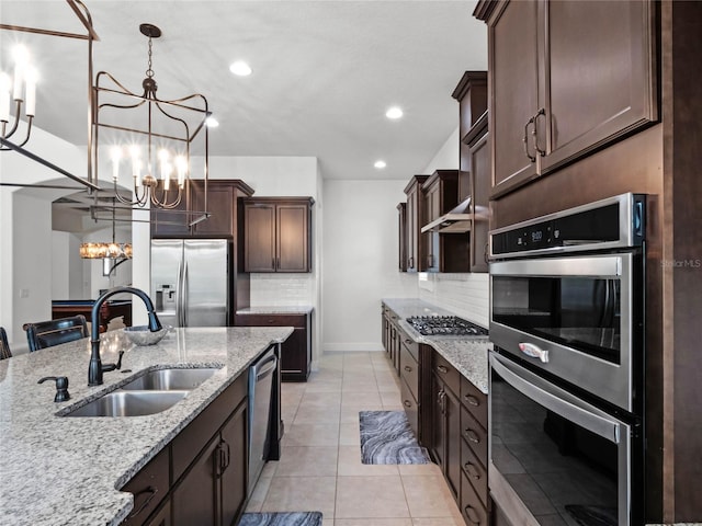 kitchen featuring sink, stainless steel appliances, light stone counters, dark brown cabinetry, and decorative light fixtures