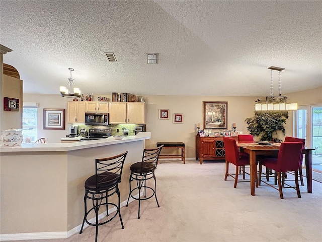 kitchen featuring backsplash, electric range, hanging light fixtures, light carpet, and light brown cabinetry