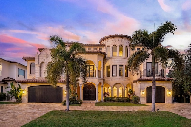 mediterranean / spanish home with a garage, decorative driveway, a tile roof, and a balcony