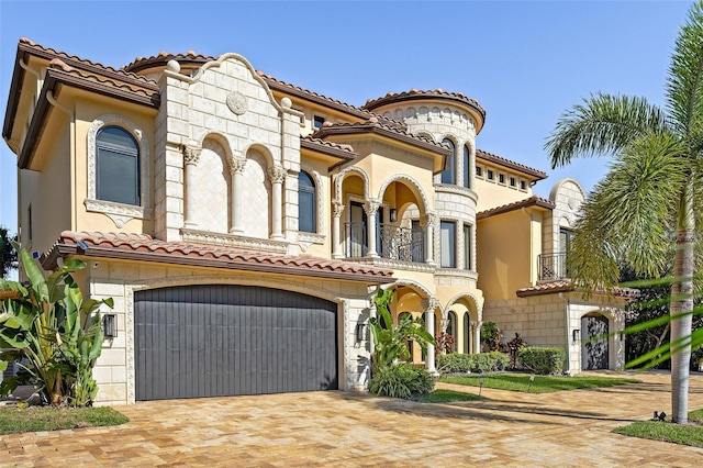 mediterranean / spanish house featuring a garage, decorative driveway, a tile roof, and a balcony