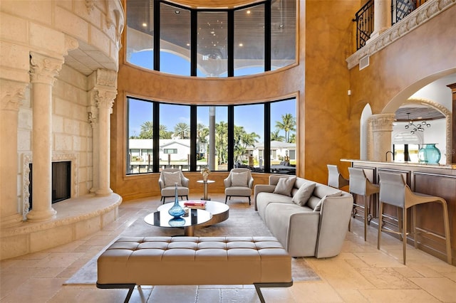 living room with arched walkways, a towering ceiling, stone tile flooring, a stone fireplace, and ornate columns