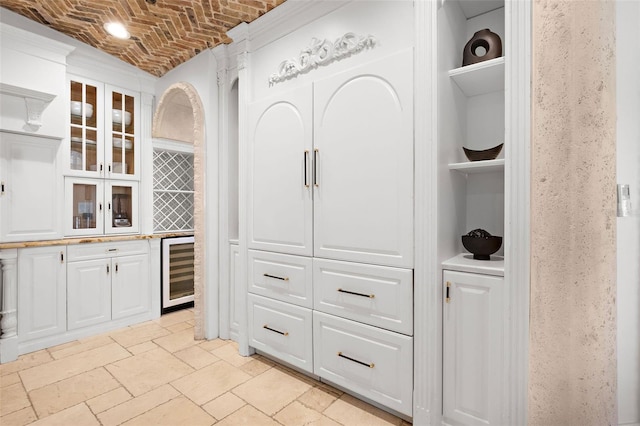 kitchen with brick ceiling, wine cooler, glass insert cabinets, and white cabinetry