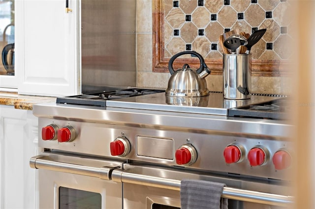 interior details featuring tasteful backsplash, light countertops, double oven range, and white cabinets