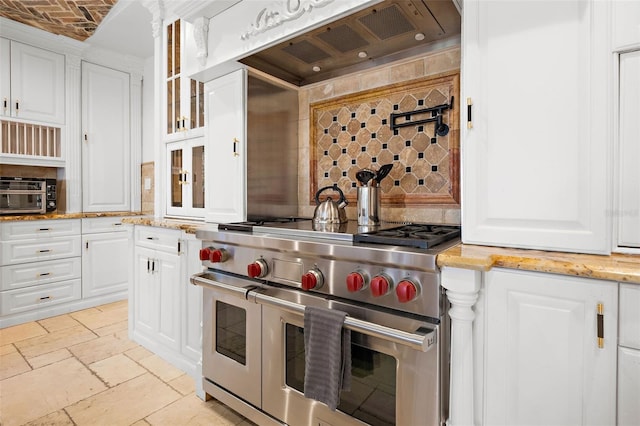 kitchen featuring stone tile floors, custom range hood, glass insert cabinets, double oven range, and white cabinetry