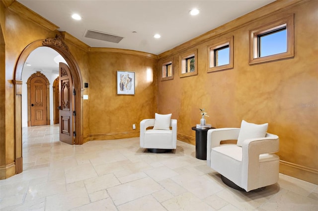 sitting room featuring arched walkways, recessed lighting, stone tile flooring, ornamental molding, and baseboards