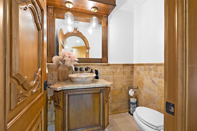 half bath with wainscoting, toilet, ornamental molding, vanity, and tile walls