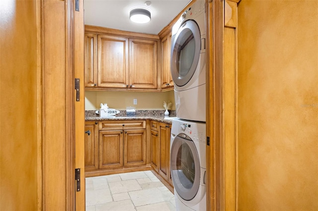 washroom featuring cabinet space, stone tile floors, and stacked washer / drying machine