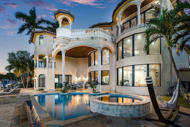 exterior space with a tile roof, stucco siding, a pool with connected hot tub, a patio area, and a balcony