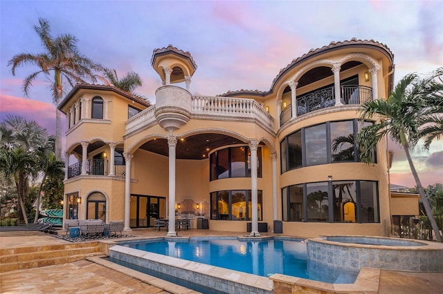 back of property at dusk with a pool with connected hot tub, a patio, a balcony, and stucco siding