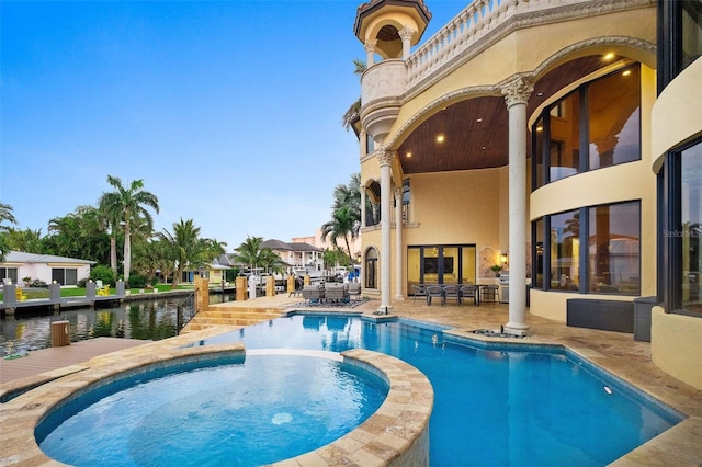 view of swimming pool with a patio area, a water view, and a pool with connected hot tub