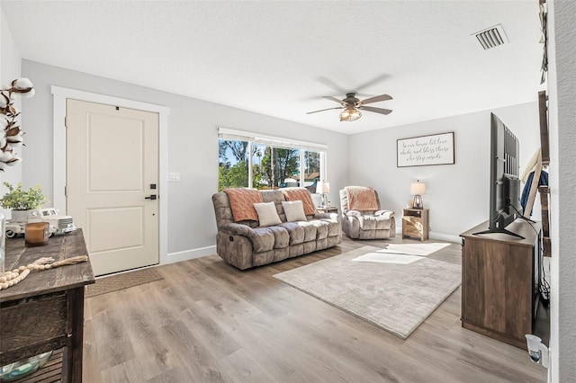 living room featuring ceiling fan, light hardwood / wood-style flooring, and a textured ceiling